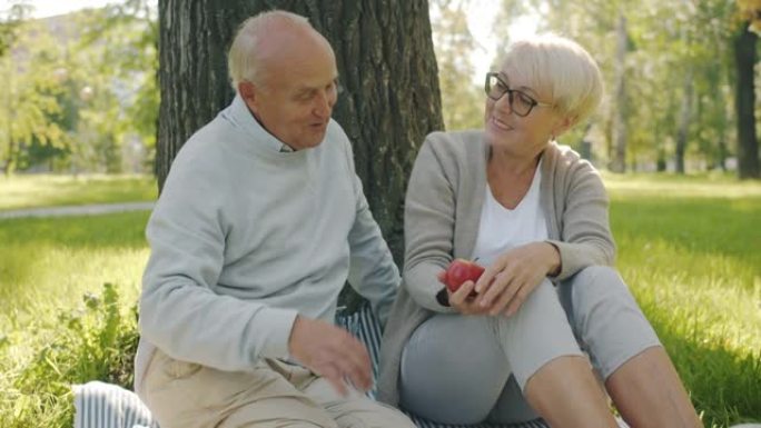 在公园野餐时，充满爱心的高级夫妇拥抱着和苹果玩得开心