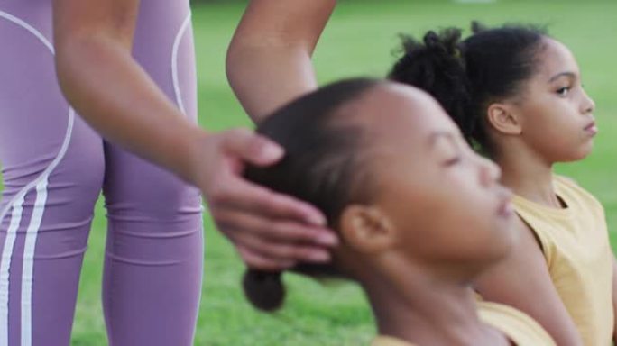 混合种族女教师在户外伸展瑜伽时纠正不同群体的学童