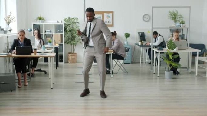 美国黑人表演者在现代办公室跳舞，而穿着西装的人在背景中工作