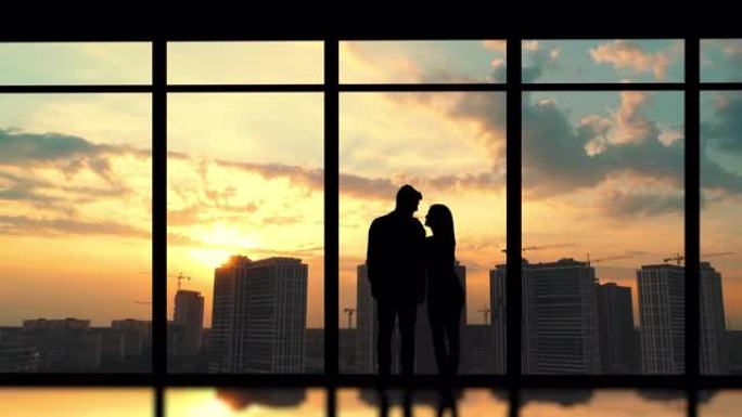 这对年轻夫妇站在建筑物背景上的窗户附近