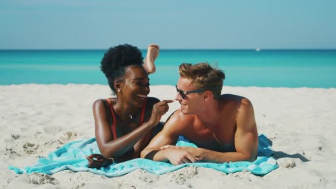 快乐的年轻不同种族的夫妇的慢动作很有趣，可以在海滩度假期间涂上防晒霜或晒黑乳液来照顾他们的皮肤。