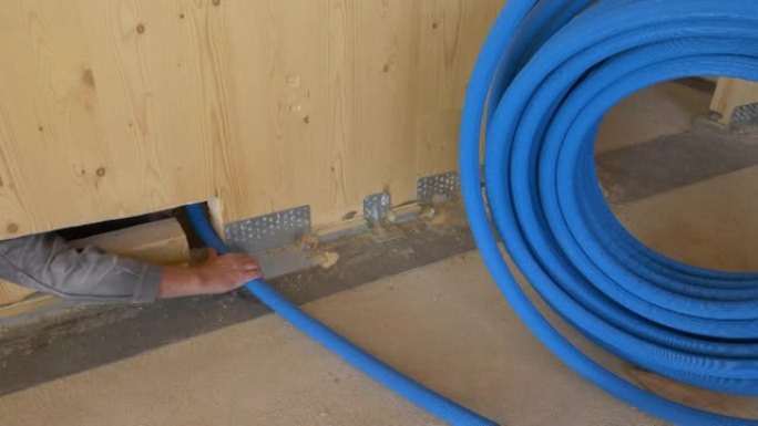 特写: 水管工将水暖管穿过硬木墙下的狭窄孔