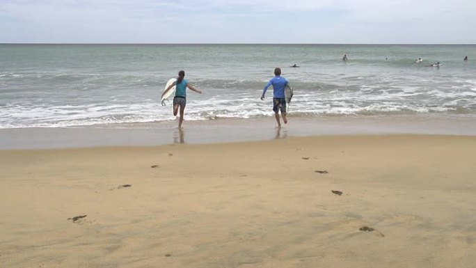慢动作: 年轻的冲浪者带着冲浪板跑进水中