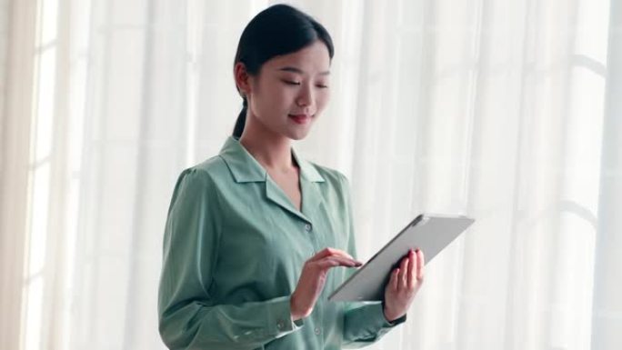 使用数字平板电脑站在窗前的年轻女企业家