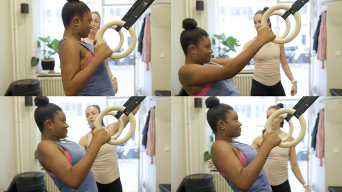 年轻女子与私人教练一起在体操戒指上锻炼