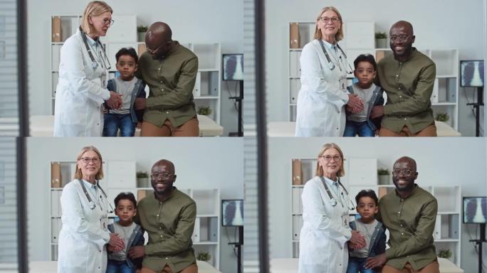 快乐的年轻人带着他的儿子和成熟的医生在诊所看着相机