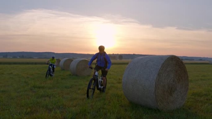 SLO MO夫妇骑自行车的人在日落时分在干草堆中骑山地自行车