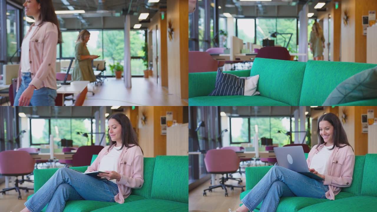 女商人带着笔记本电脑走过办公室，然后坐在现代办公室的休息座位区，以慢动作拍摄