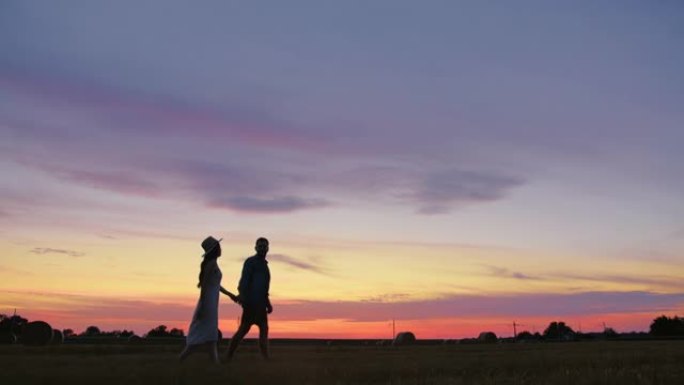 追踪成年夫妇在田野里走到日落时牵手的慢动作镜头