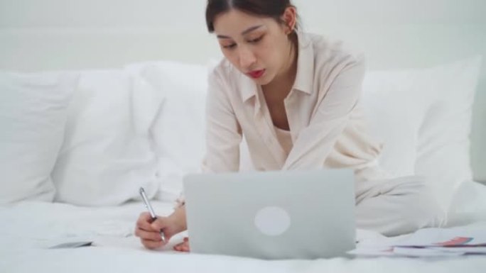 亚洲女商人使用科技平板电脑工作，并在床上写笔记本