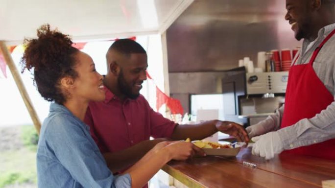 微笑的非洲裔美国男性餐车老板为快乐的不同类型的夫妇提供食物