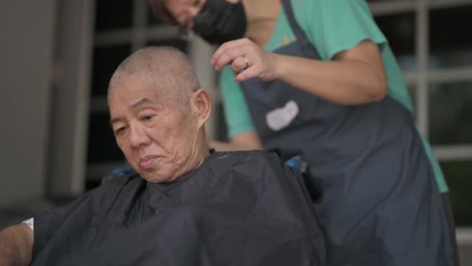 坐在轮椅上的亚洲华裔高级男子在他家前院理发