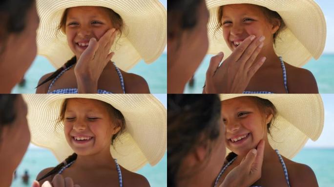 年轻母亲的特写镜头正在她的小快乐微笑的女儿脸上涂抹防护防晒霜或防晒霜，以护理海边海滩上的皮肤