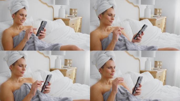 熟女躺在床上穿毛巾在家看手机笑