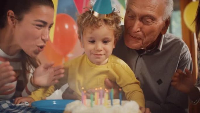 庆祝一个可爱的小男孩生日的幸福家庭肖像: 母亲和祖父帮助孩子吹灭蛋糕蜡烛，而其他孩子则欢呼和鼓掌。童