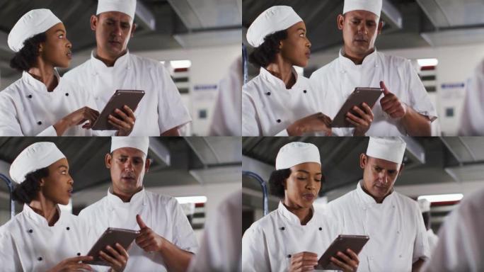 两位不同的男女厨师在餐厅厨房里交谈和使用平板电脑