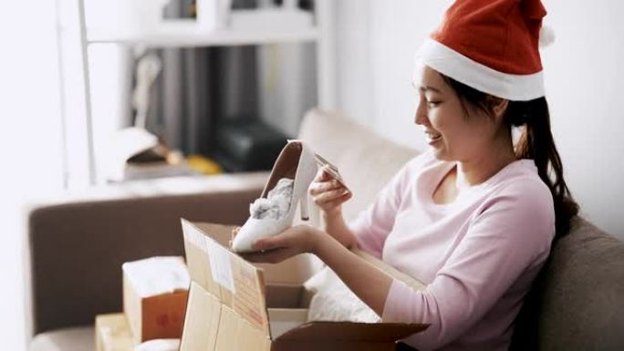 亚洲女性消费者打开纸板箱在圣诞节期间获得邮政包裹，在线购买鞋子