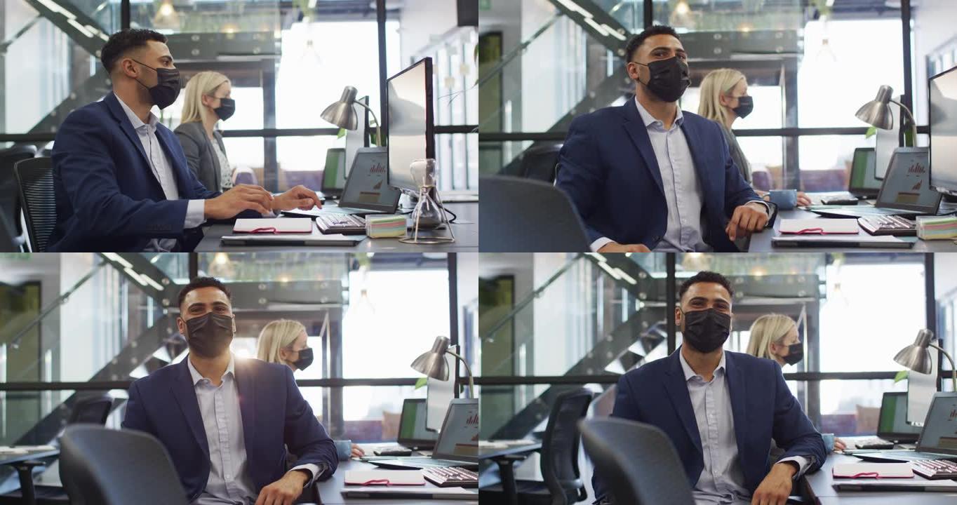 混血商人戴着口罩并与同事在后台工作时使用计算机