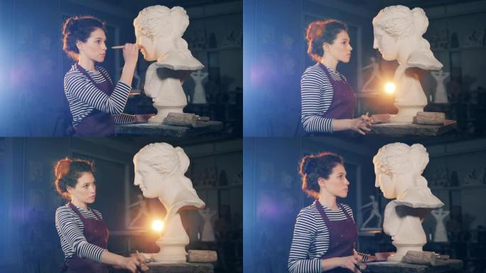 Lady artist正在用刷子照顾石膏雕塑。艺术概念，艺术家在设计工作室工作。