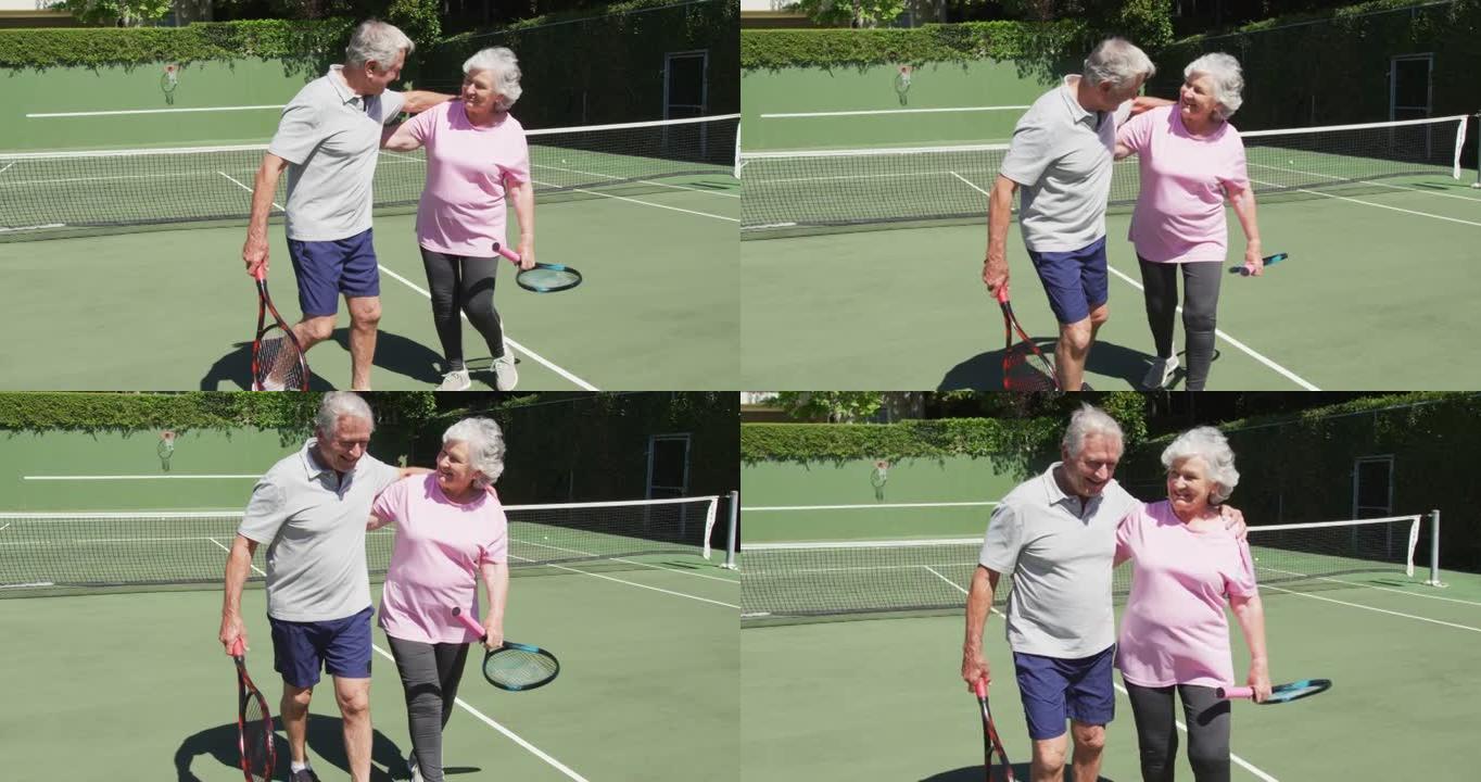 快乐的高加索高级夫妇在玩游戏后在阳光下的户外网球场拥抱