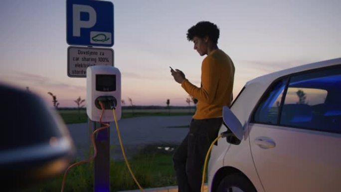 SLO MO young男子黄昏时在停车场上充电电动车