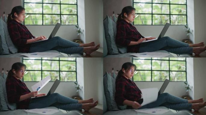 亚洲妇女坐在沙发上在家用笔记本电脑工作