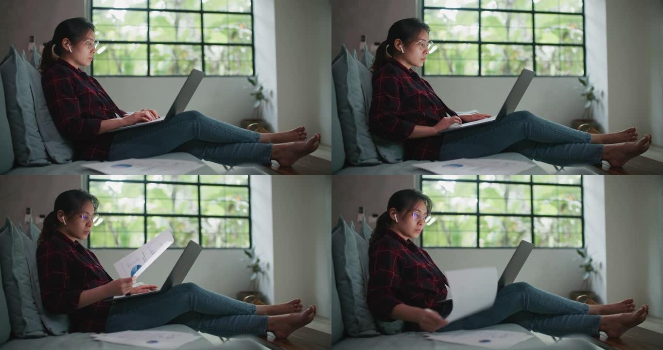 亚洲妇女坐在沙发上在家用笔记本电脑工作