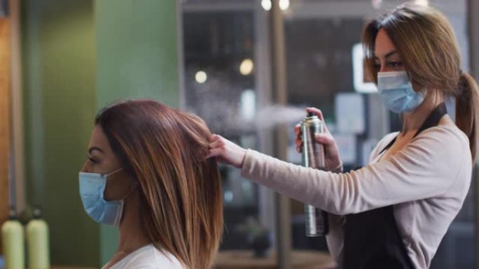 美发店的女性美发师戴着口罩在女性顾客的头发上喷洒发胶