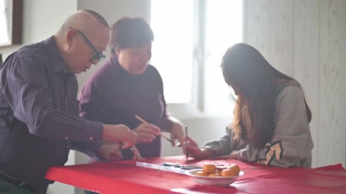 亚洲华人家庭在红纸上书写中国书法，以繁荣并准备农历新年家居装饰
