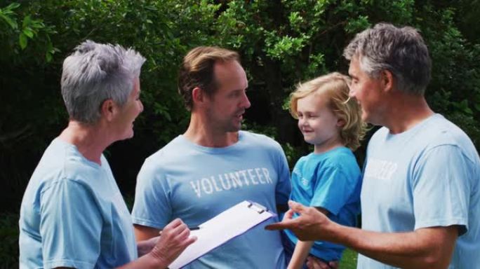 一对白人老夫妇和父子穿着志愿者t恤在田野里交谈