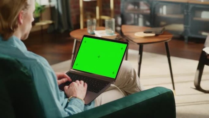 年轻的成年男子在带绿屏模拟显示的笔记本电脑上的家庭阁楼公寓工作。有创造力的男性浏览网络，在社交媒体上