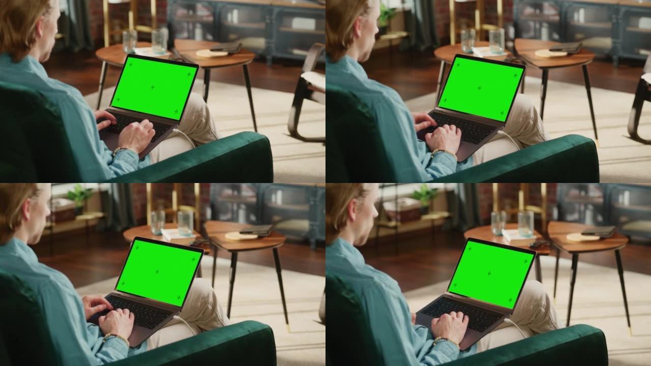 年轻的成年男子在带绿屏模拟显示的笔记本电脑上的家庭阁楼公寓工作。有创造力的男性浏览网络，在社交媒体上