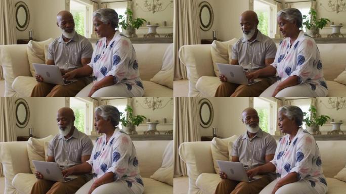 非裔美国老年夫妇坐在家里的沙发上一起使用笔记本电脑