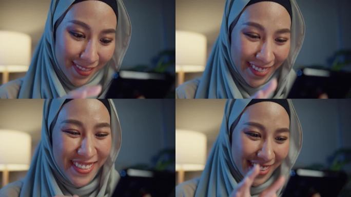 特写迷人开朗的年轻亚洲穆斯林美女戴着头巾，随意坐在沙发上，晚上在家里的客厅享受网上购物。女孩伊斯兰生