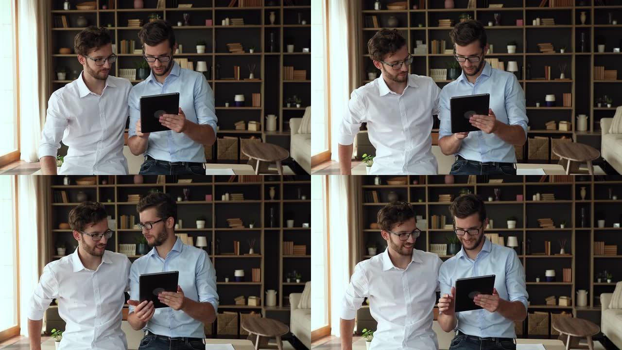 千禧一代的双胞胎兄弟站在桌子旁聊天，看着平板电脑