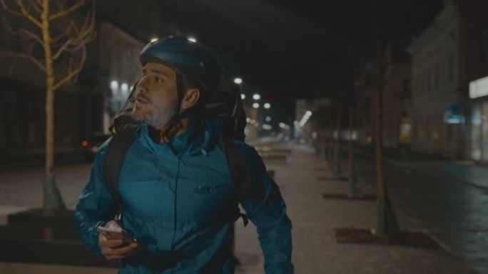 送餐男孩在夜间使用手机在城市街道上搜索地址时奔跑