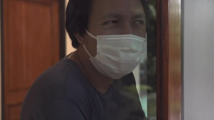 亚洲男子透过窗户自我检疫寻找冠状病毒或新型冠状病毒肺炎