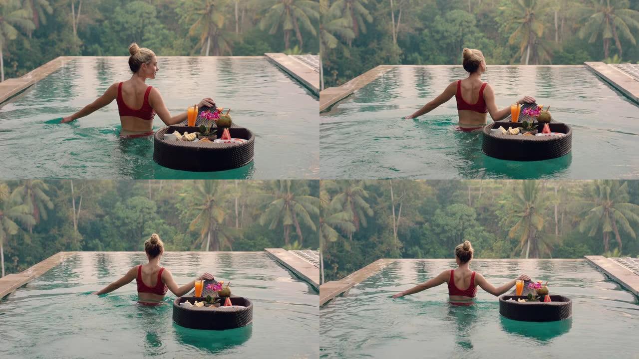 美丽的女人在游泳池吃早餐，在豪华酒店水疗中心享受异国美食，可以看到热带丛林