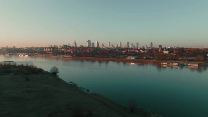 无人机在宽阔的维斯拉河上空升起，在晴朗的蓝色日出天空下展现美丽宁静的华沙城市景观。