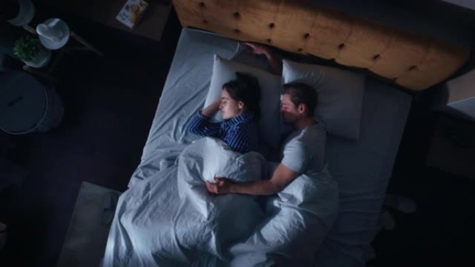 顶视图家: 幸福的年轻夫妇晚上在床上睡觉拥抱在一起。漂亮的女朋友和帅气的男朋友睡在一起。两口之家甜蜜