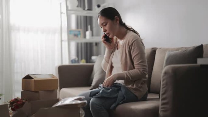亚洲女性消费者感觉不好坐在沙发上，在网上与商店联系，询问家里有问题的产品订单，电话投诉。