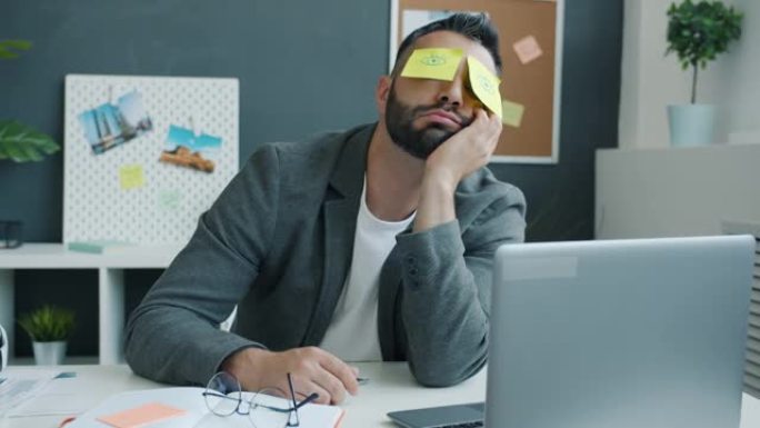 效率低下的上班族在工作场所的办公桌上睡觉，便签上露出睁开的眼睛