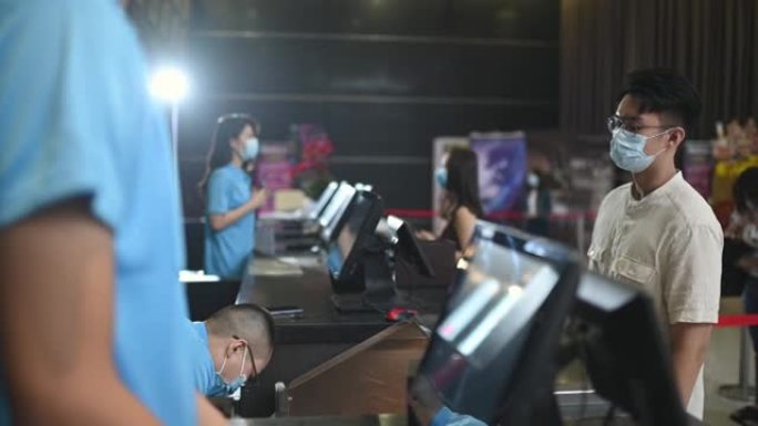 亚洲华人年轻人戴着面具在电影院放电影前买爆米花