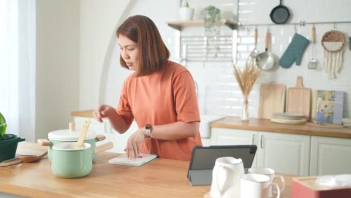 女人在家里的厨房里用数字平板电脑做饭和学习