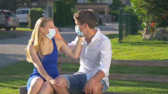 特写: 夫妇坐在公园长椅上时戴着面具调情和亲吻。