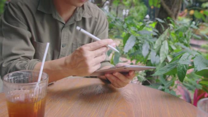亚洲男子在户外咖啡馆的数字平板电脑上撰写投资计划