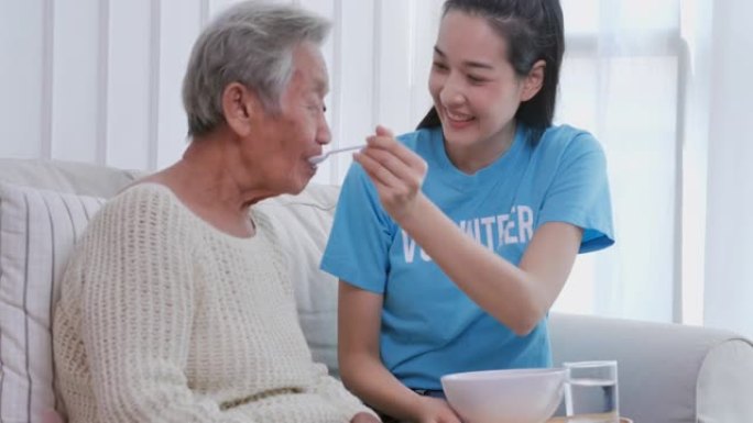 亚洲年轻女性志愿者帮助在疗养院为82岁的亚洲老年祖母提供早餐。在家护理人员