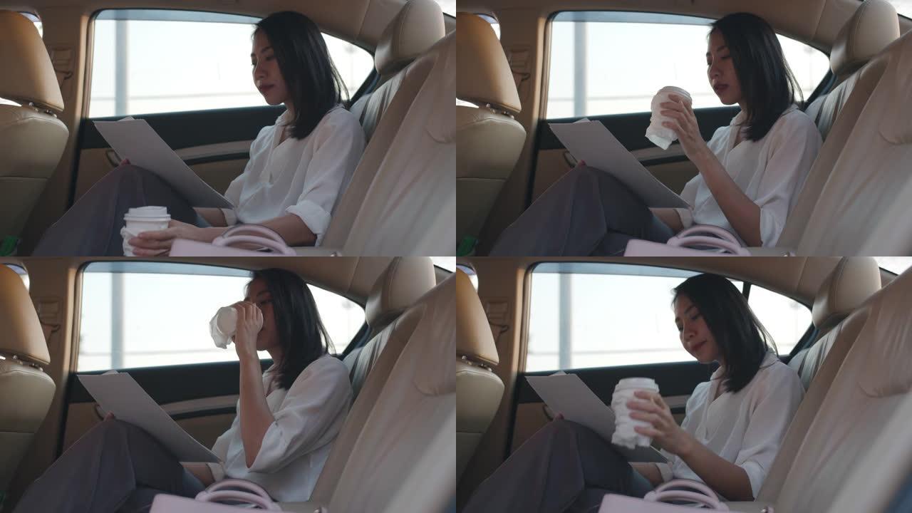 亚洲女商人穿着时尚的办公室衣服，早上在城市现代城的汽车后座上工作和喝一次性纸杯热饮。