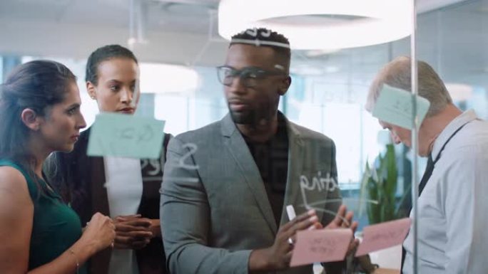 使用便笺的多元化商人非裔美国人团队负责人与致力于解决方案的同事集思广益，讨论在办公室会议4k上在玻璃