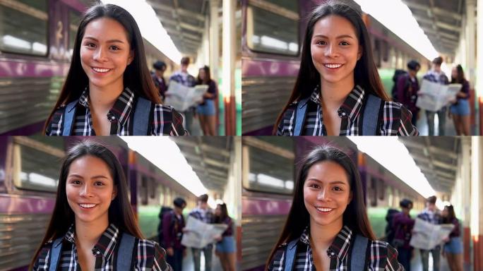 美丽的年轻亚洲游客独自旅行，独自在火车站散步。她和后面的朋友对着镜头微笑，讨论了这次旅行。